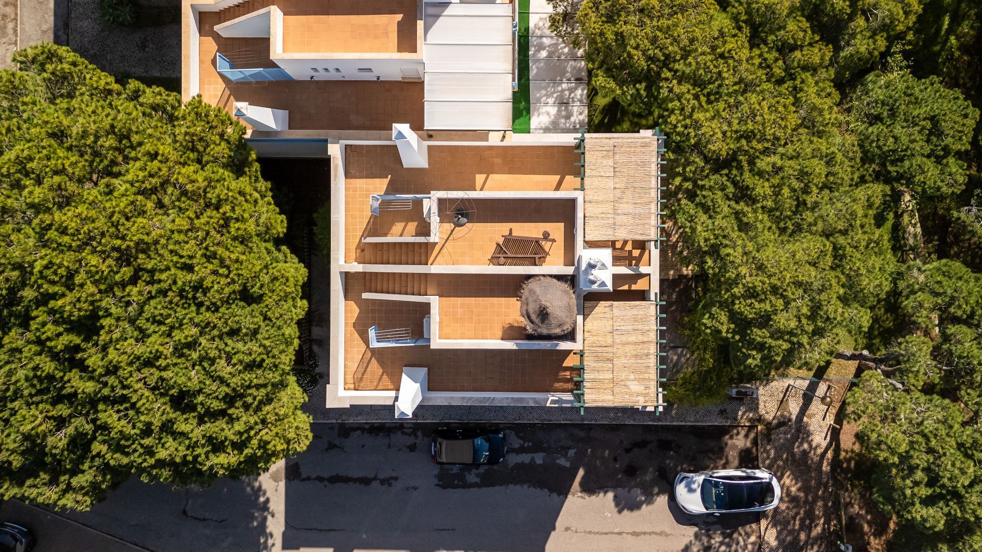 An aerial view of a modern two-story building with a flat roof, a covered outdoor area with a wooden deck, and a car parked in front.