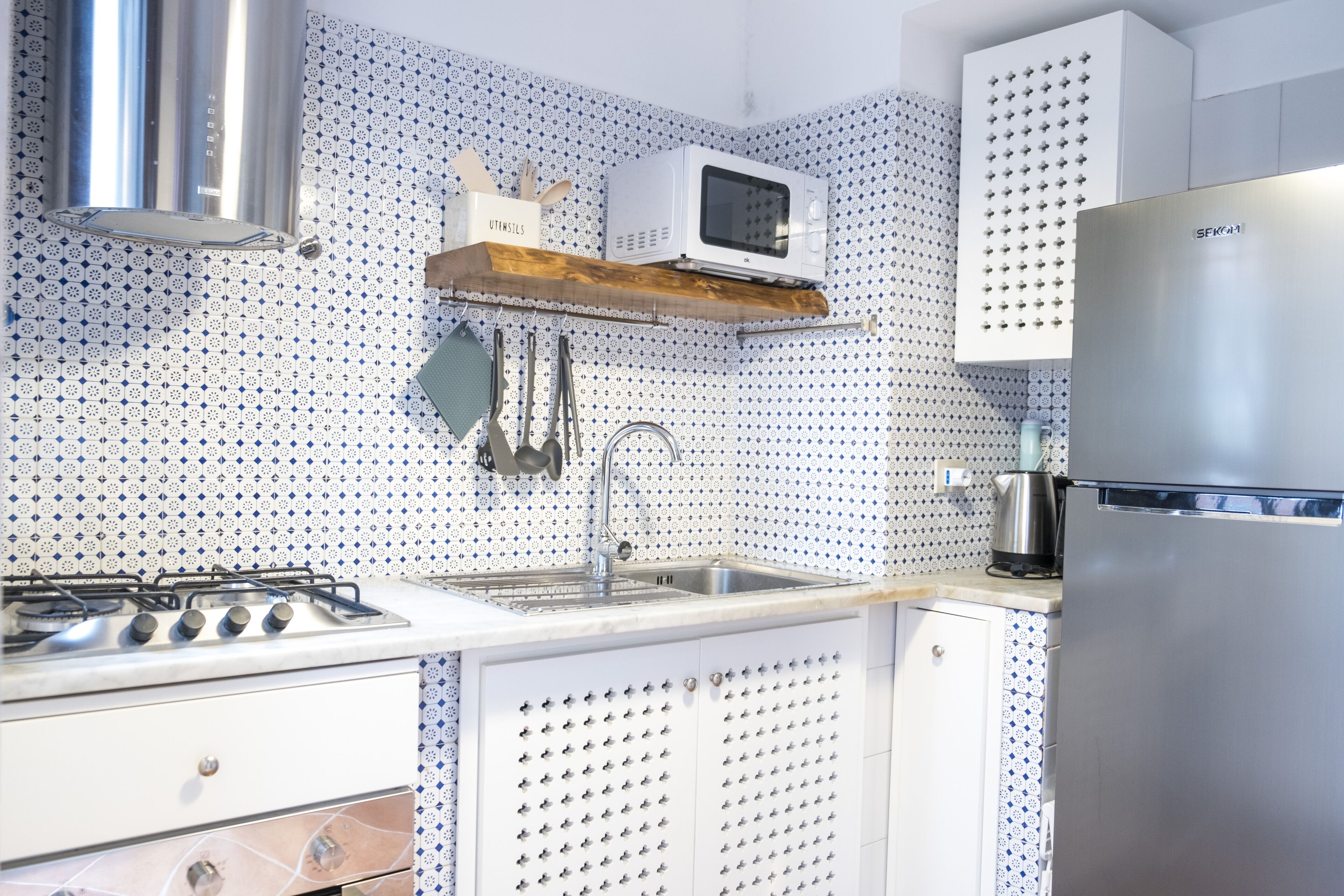 Cocina moderna con estufa a gas, electrodomésticos de acero inoxidable, salpicadero con diseño y utensilios colgantes.