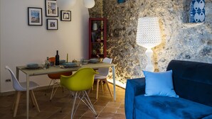 A dining area with a stone wall, a table set with plates and glasses, and a blue sofa with a cushion. - House Garden San Lorenzo (Salerno)