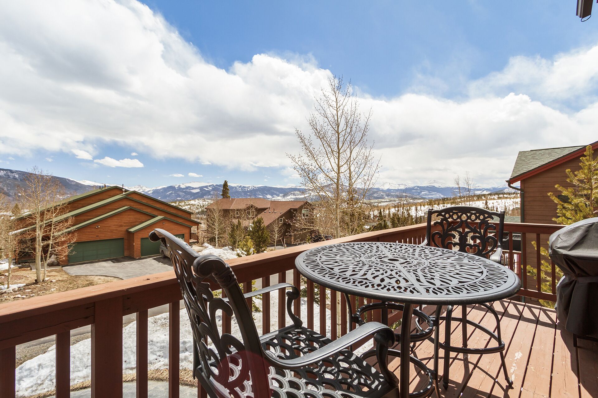 A wooden deck with a metal table and chairs, overlooking a snowy mountain landscape.