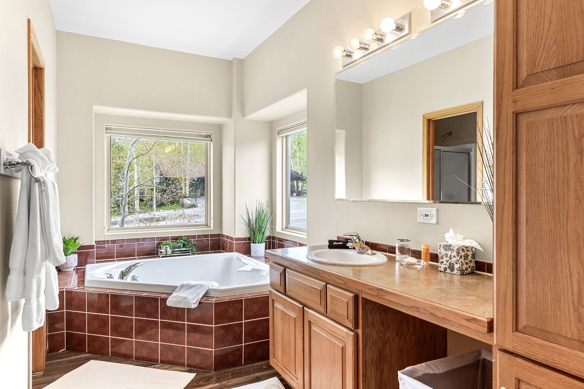 A modern bathroom with a large bathtub, a vanity with a sink, and a mirror above the sink. There are windows providing natural light and a view of the outdoors.