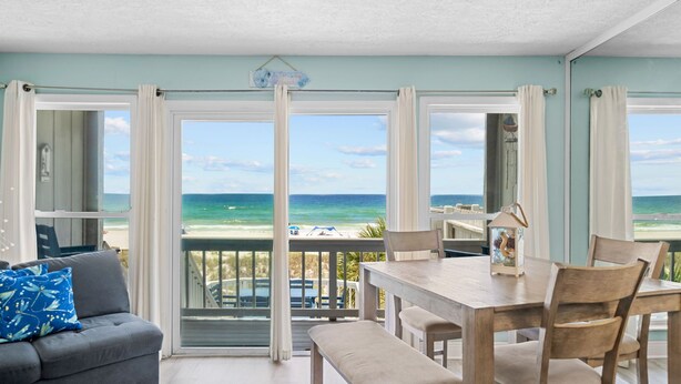 A balcony with a view of the ocean, a dining table with chairs, and a sofa with a cushion.
