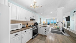 A modern kitchen with white cabinets, a stainless steel sink, and a view of the ocean.