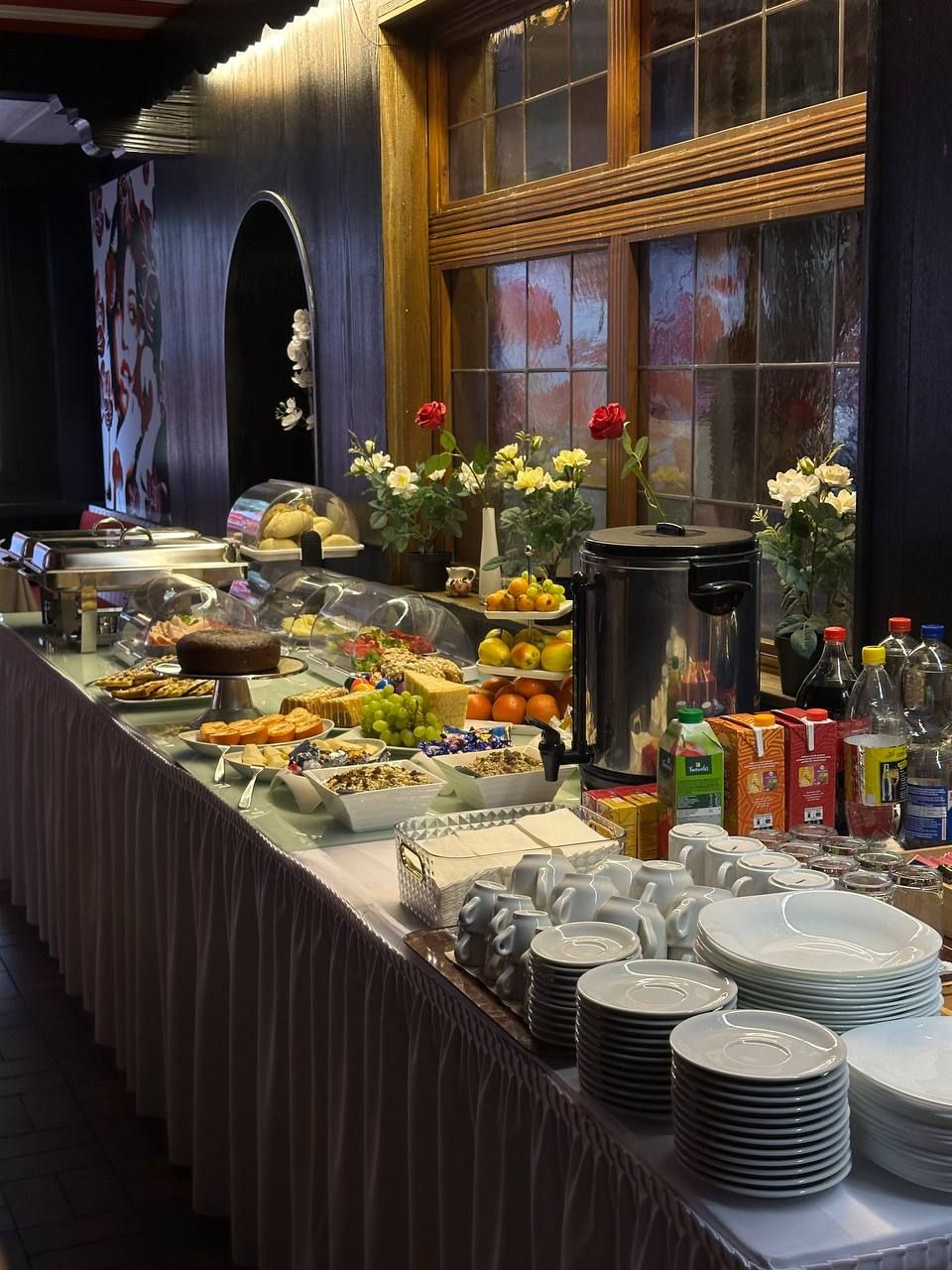 A buffet setup with various food items, a coffee maker, and a selection of plates and cups.