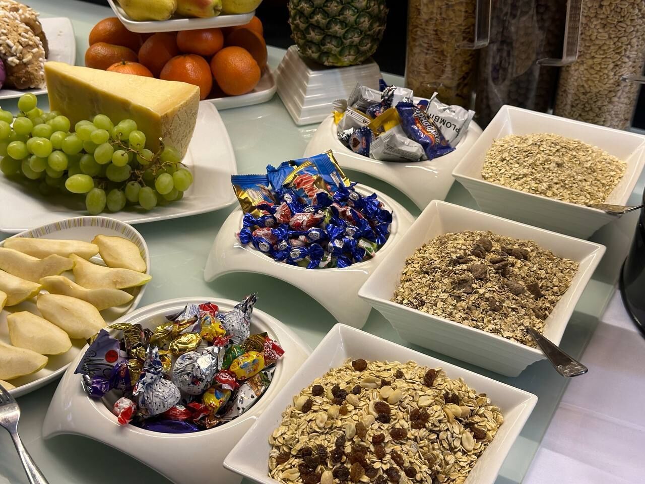 Una mesa de buffet con diversos alimentos, incluyendo queso, uvas, caramelos variados y granola.