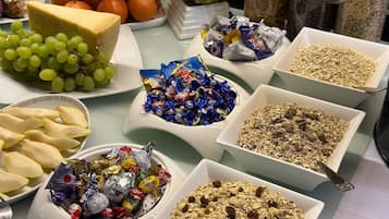 Una mesa de buffet con diversos alimentos, incluyendo queso, uvas, caramelos variados y granola.