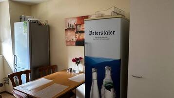A dining area with a wooden table, chairs, a refrigerator, and a poster of Peterstaler mineral water.