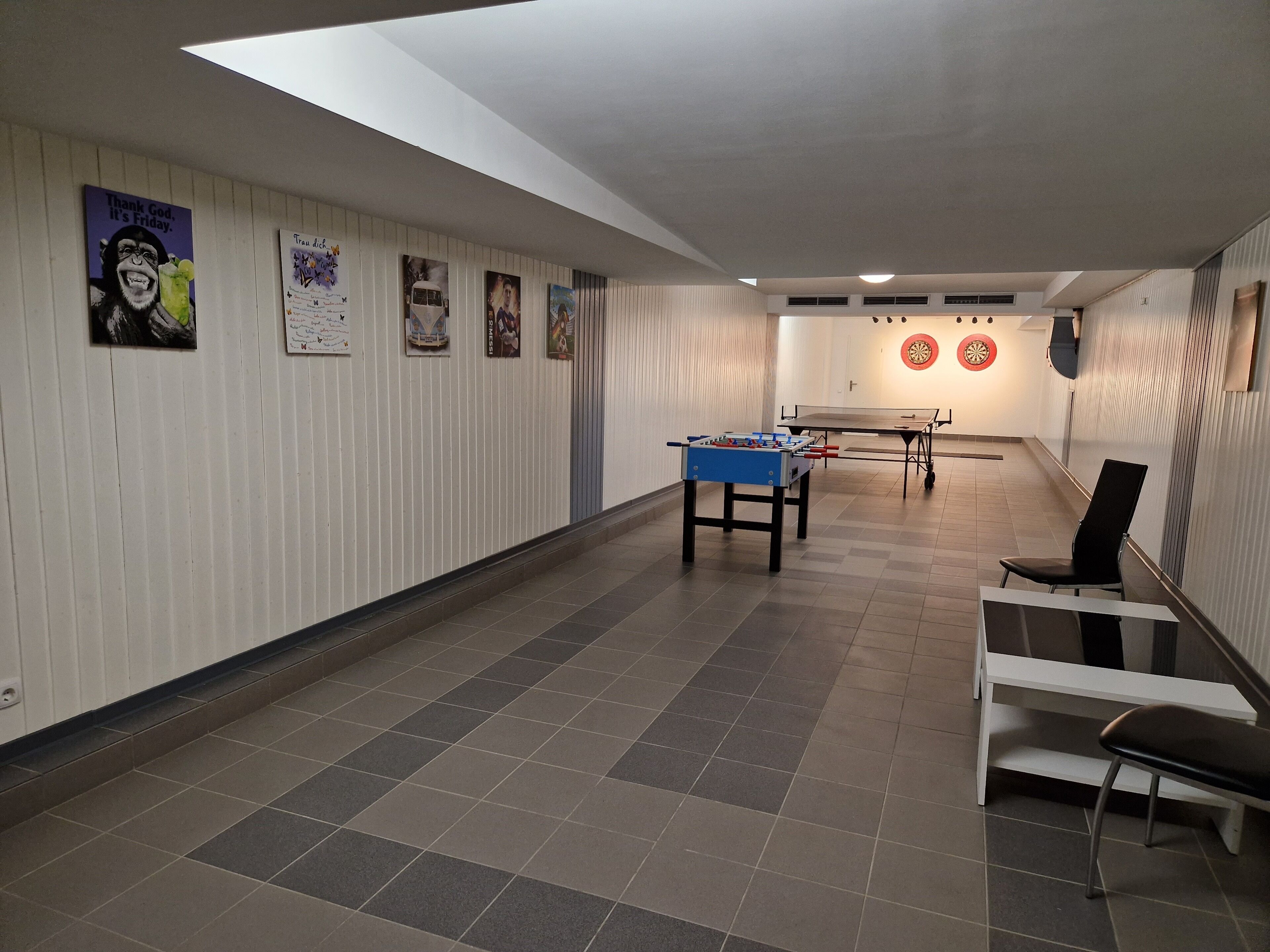 Un pasillo con mesa de fútbolín, mesa de ping pong y dardos.