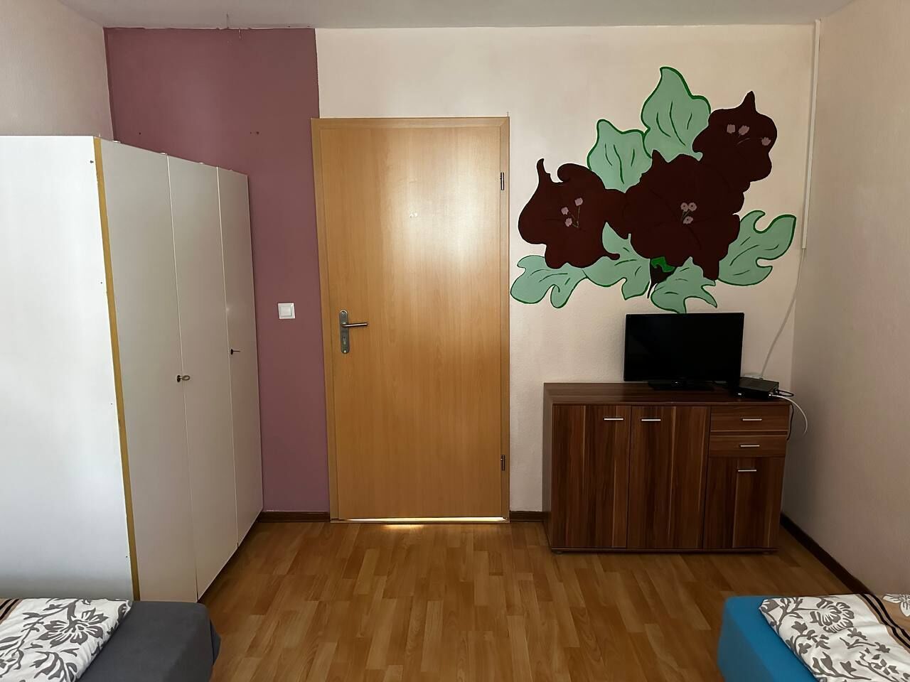 Una habitación con piso de madera, un armario, un mueble con televisor y un adorno en la pared.