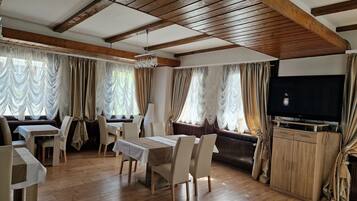 Comedor con vigas de madera, televisor y cortinas.