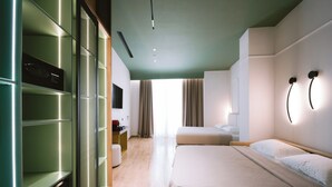 A modern hotel room with a large bed, a wardrobe with a mirror, a desk with a chair, and a view of the street through the window. - Hotel Noemie (Himarë)