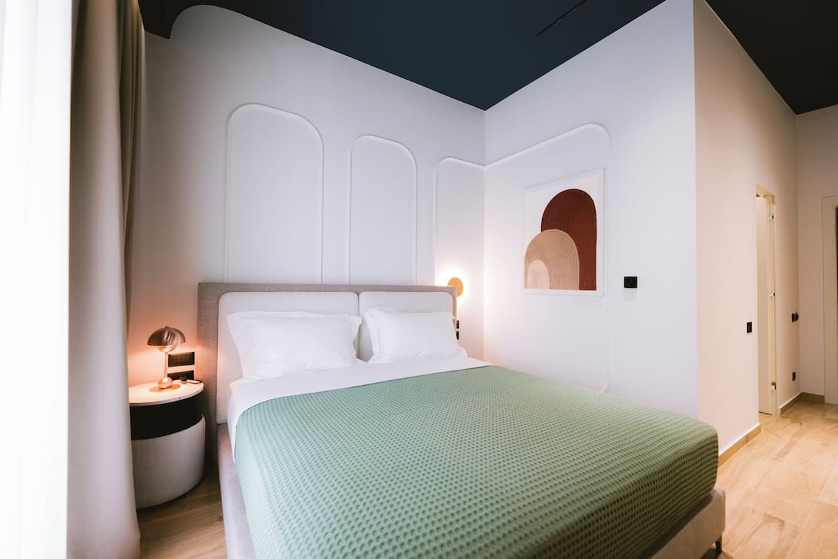 A modern bedroom with a large bed, a round bedside table, and a wall-mounted mirror.