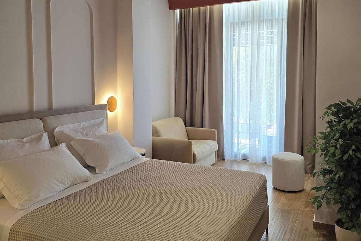 A modern hotel room with a large bed, a sitting area, and a view of the outdoors.