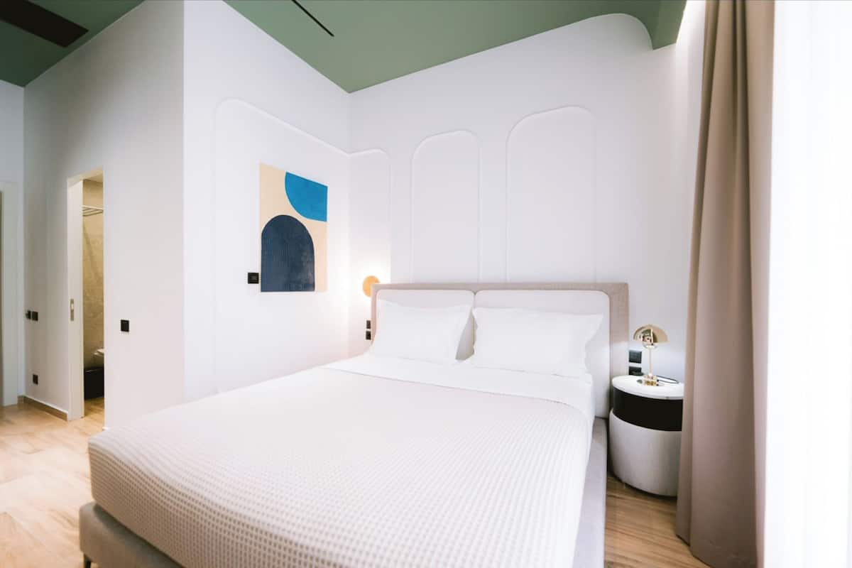 A modern bedroom with a large bed, a bedside table, and a wall-mounted light.