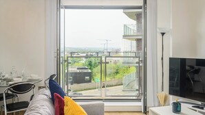 A modern living room with a large TV, a sofa with colorful cushions, a dining area with a table and chairs, and a sliding glass door leading to a balcony with a view of the city. - Charming 1-bed Apartment in Leeds (Leeds)