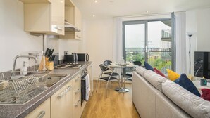 A modern kitchen with a dishwasher, sink, and stove. There is a dining area with a table and chairs, and a sofa with colorful cushions. - Charming 1-bed Apartment in Leeds (Leeds)