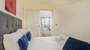A modern bedroom with a large bed, a grey upholstered headboard, and a view of a balcony with a white sofa. - Charming 1-bed Apartment in Leeds (Leeds)