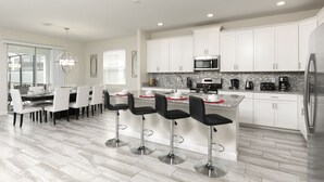 A modern kitchen with white cabinets, a stainless steel refrigerator, and a central island with bar stools. - Luxury 6BR Townhome with Private Pool, Game Room & Resort Access Near Disney (Kissimmee)