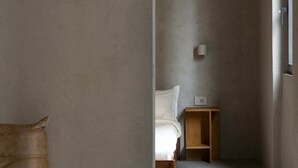 Ein schmaler Flur, der in ein Schlafzimmer mit Bett, Nachttisch und Wandleuchte führt.