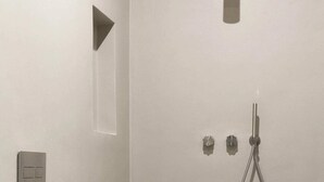 Ein modernes Badezimmer mit Toilette, einer Dusche inklusive Duschhandstück und einer wandmontierten Leuchte.