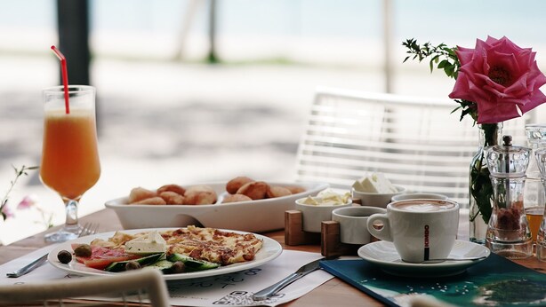 A table with breakfast items, a glass of orange juice, and a pink flower. - Himara 28 (Himarë)