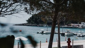 A marina with boats docked, a sandy beach, and a rocky island in the background. - Himara 28 (Himarë)