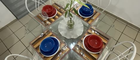 A dining table with four chairs, a central vase with a plant, and a tiled floor.