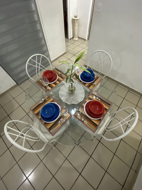 A dining table with four chairs, a central vase with a plant, and a tiled floor.