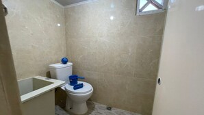 A small bathroom with a toilet, a blue cleaning brush, and a blue globe on the tank. - Hotel O Kng Homestay Syariah (Pekanbaru)
