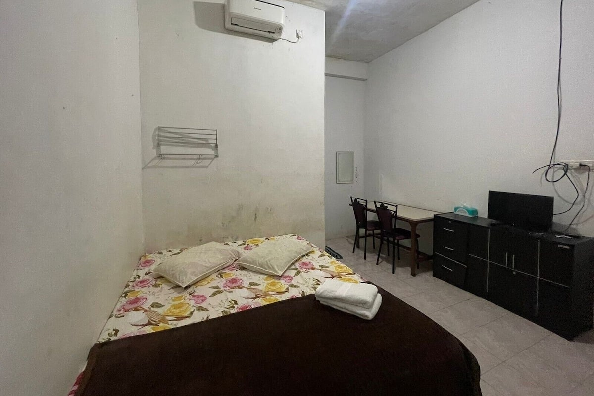 Una habitación pequeña y poco amoblada con una cama, un escritorio, una silla y un televisor.
