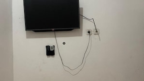 A flat-screen TV mounted on a white wall with a power cord and a power strip. - Hotel O Kng Homestay Syariah (Pekanbaru)