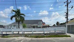 A commercial building with a fenced parking area, a palm tree, and a clear sky. - Hotel O Kng Homestay Syariah (Pekanbaru)