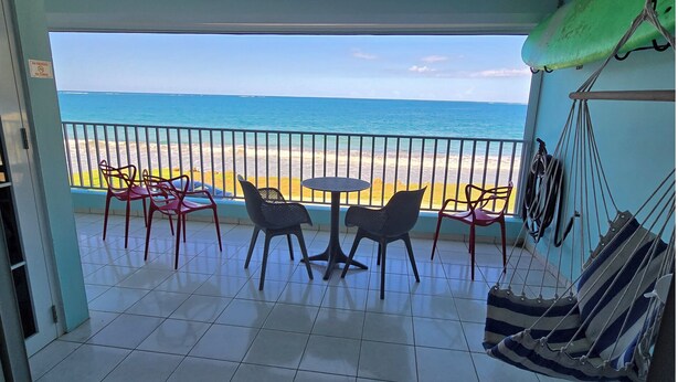 Un balcone con vista sulla spiaggia, un tavolo con sedie e un'amaca.