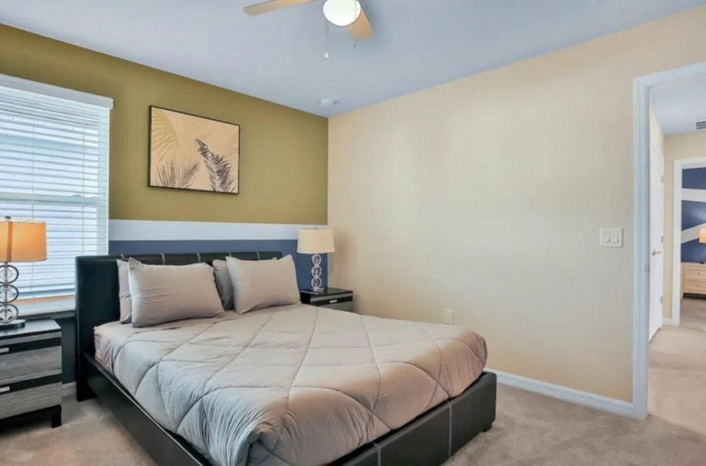 Un dormitorio con cama, mesitas de noche, ventilador de techo y ventana con persianas.