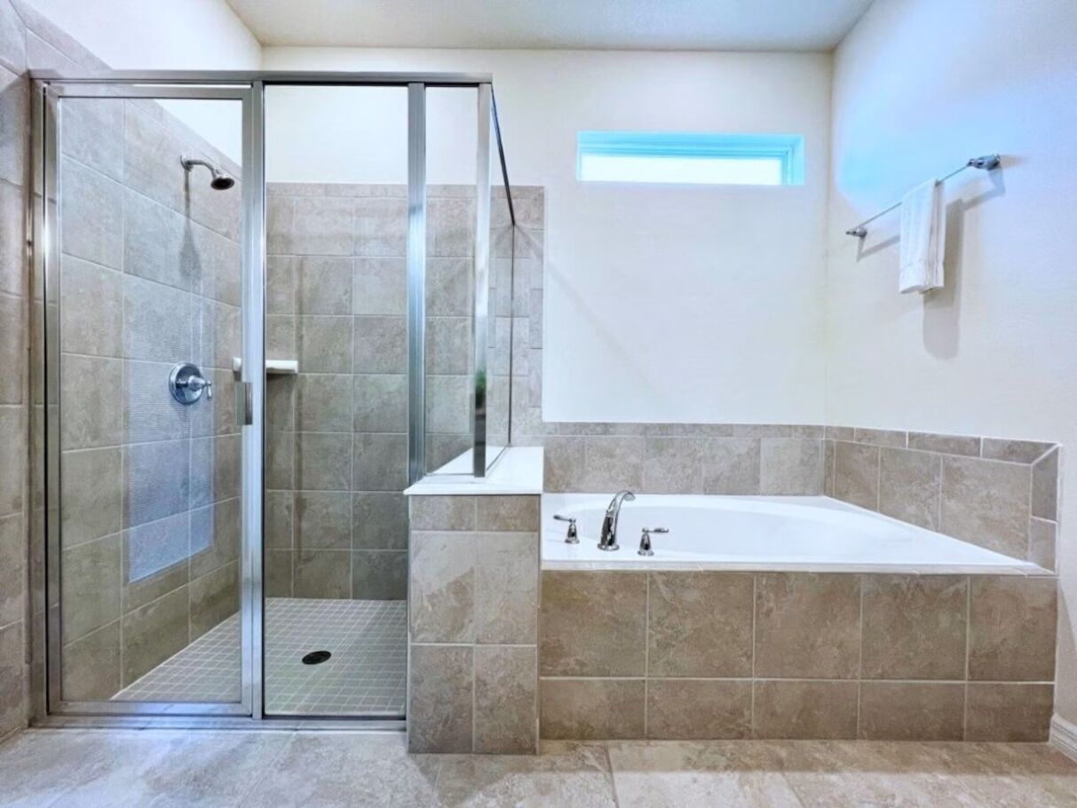 Un baño con ducha de vidrio, una bañera independiente y un ventanal que proporciona luz natural.