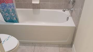 A bathroom with a white bathtub, a toilet, and a shower curtain.