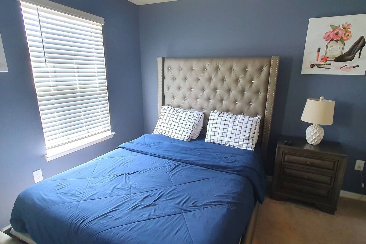 Een slaapkamer met een bed, nachtkastje, lamp en kunst aan de muur.
