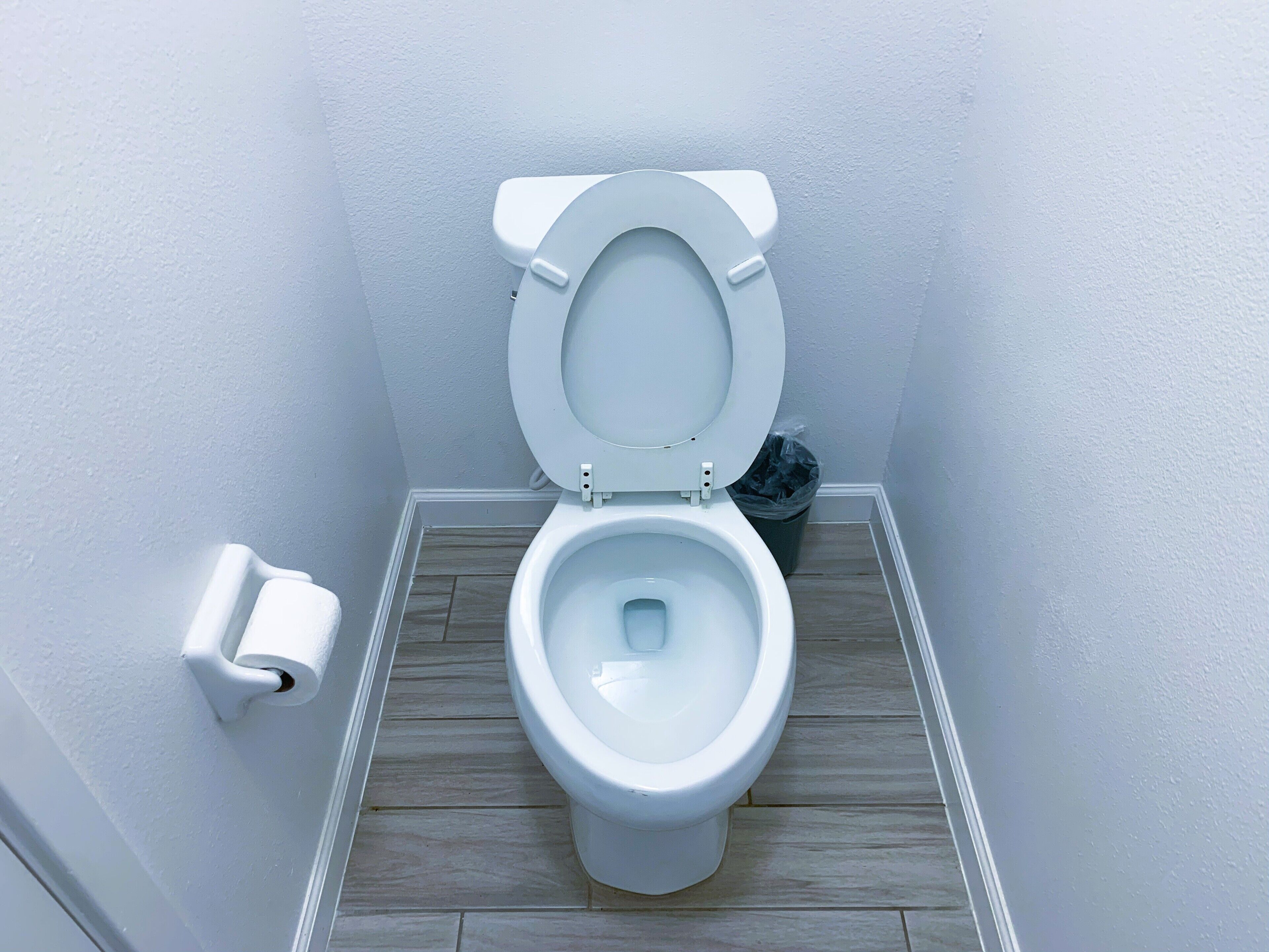 A small, modern bathroom with a white toilet, a wooden floor, and a white wall.