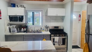 A modern kitchen with white cabinets, a stainless steel microwave, a coffee maker, and a gas stove.