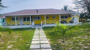 A yellow building with a tiled roof, a covered porch, and a stone pathway leading to the entrance.