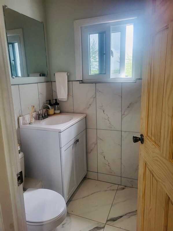 A compact bathroom with a white sink, a mirror, a toilet, and a window above the sink.