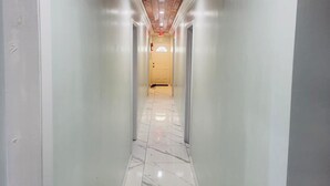 A hallway with white walls, a wooden ceiling, and a marble floor.