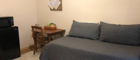 Una camera da letto con un letto, una scrivania, una sedia, un forno a microonde e una bacheca.