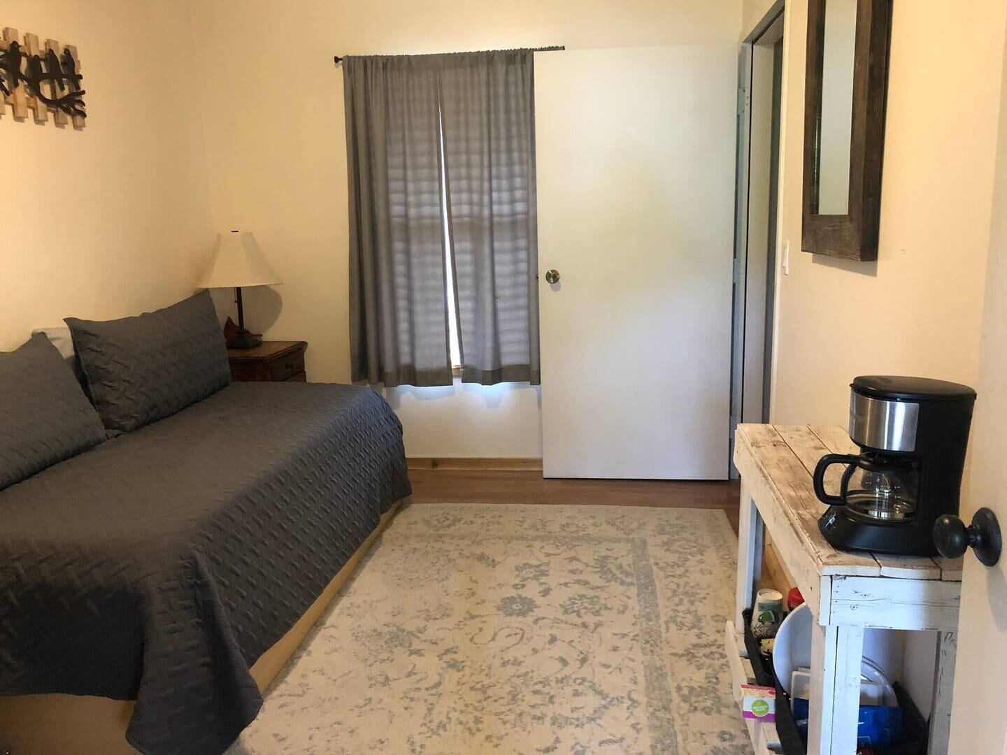 A bedroom with a bed, a nightstand, a lamp, a coffee maker, and a door.