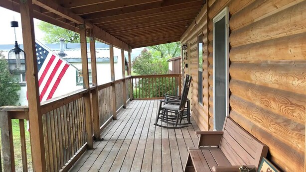 A wooden deck with a covered area, a rocking chair, a bench, and a sign that reads "Gone fishin' be back someday". - Cabin #2 - Backyard Bunkhouse
 (Irwin)
