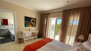 A bedroom with a bed, a desk, a chair, a window with curtains, and a painting on the wall.