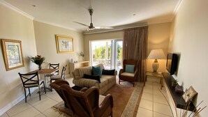 A living room with a sofa, armchairs, a dining table with chairs, a television, and a ceiling fan.