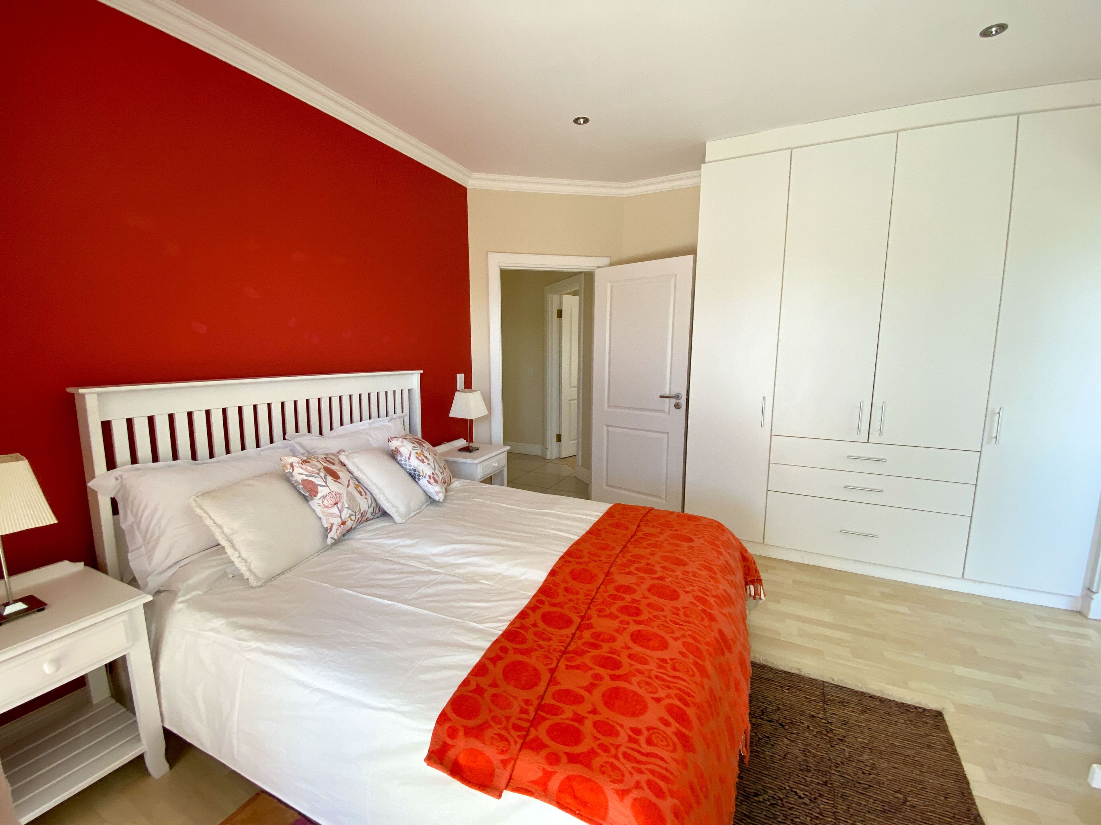 A bedroom with a white bed, red walls, and a wardrobe.