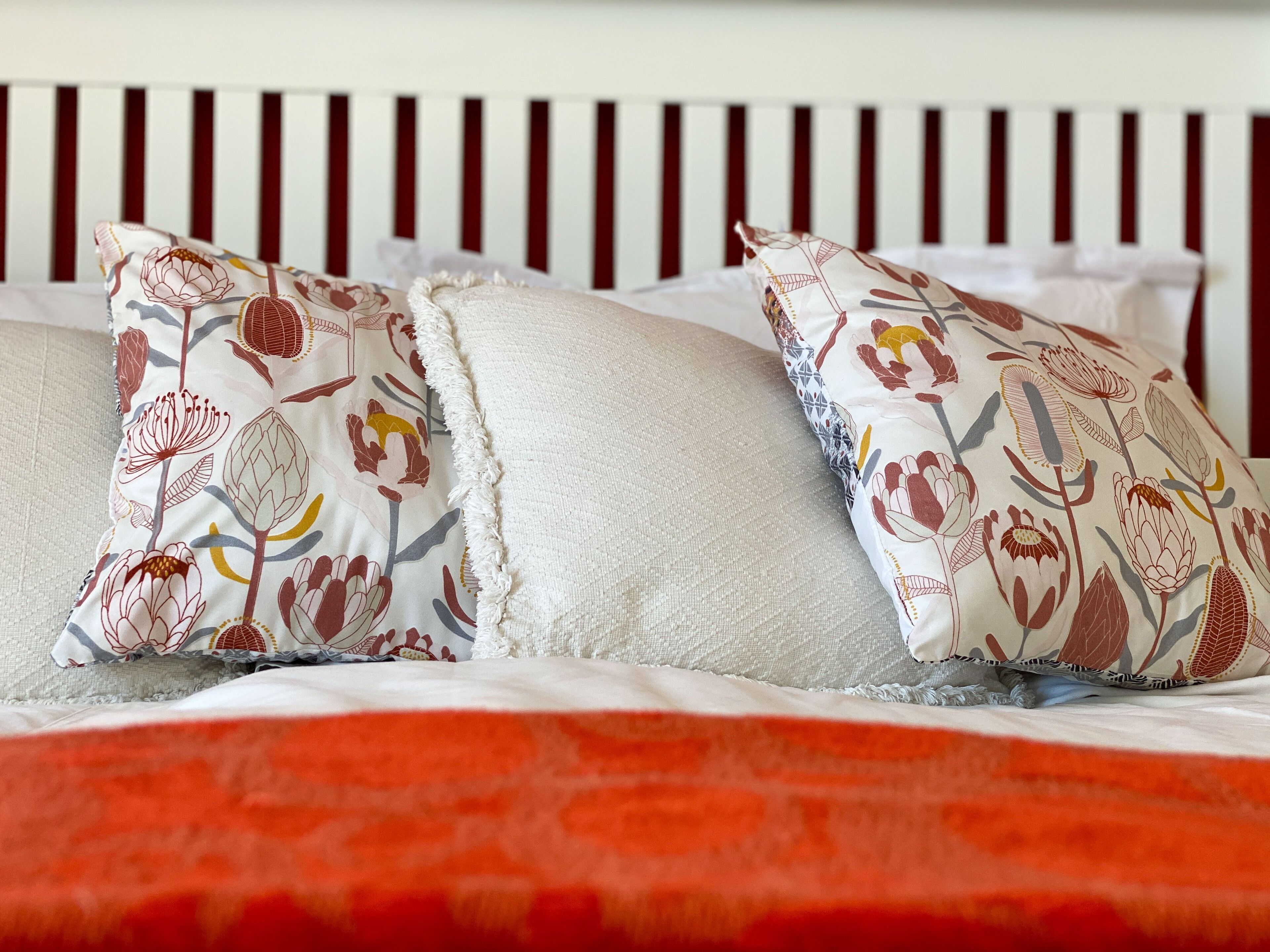 A bed with two decorative pillows and a red blanket.