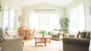 Un salon lumineux avec un ventilateur de plafond, une table ronde en bois et une grande fenêtre avec des rideaux.